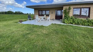 Une maison moderne avec un patio, un petit jardin et le chiffre « 2 » sur la porte.