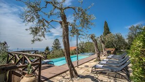 Uma área à beira da piscina com espreguiçadeiras, um cercado de madeira e vista para o mar.