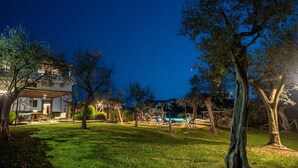 Uma área externa bem iluminada com piscina, espreguiçadeiras e um espaço de estar coberto.