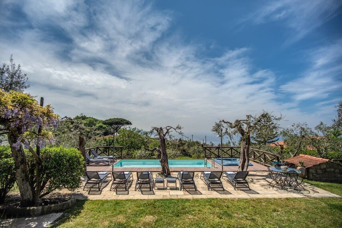 A poolside area with lounge chairs and a swimming pool, surrounded by trees and a clear sky.