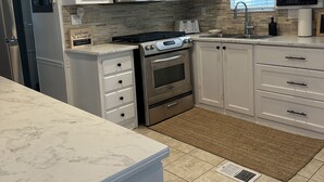 Una cocina moderna con armarios blancos, microondas de acero inoxidable, horno empotrado y un lavamanos.