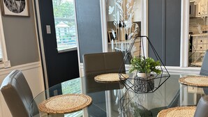 Un comedor moderno con una mesa de vidrio rodeada de sillas de cuero, con individuales tejidos y una planta en maceta.