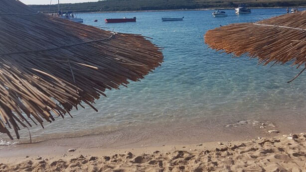 Una playa con agua cristalina, barcos y sombrillas de paja.