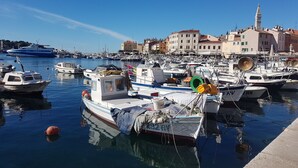 Un puerto deportivo con varias embarcaciones amarradas, un cielo azul despejado y edificios al fondo.