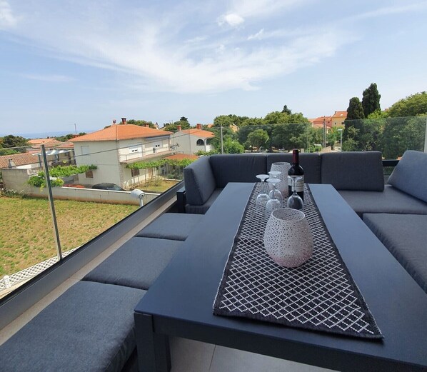 A rooftop terrace with a table set for dining, overlooking a residential area with houses and trees.