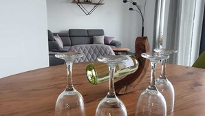 Una mesa de comedor con cuatro copas de vino y una botella verde. Un sofá gris y una pieza decorativa se ven al fondo.