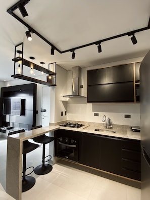 A modern kitchen with a central island, black cabinetry, stainless steel appliances, and pendant lighting.
