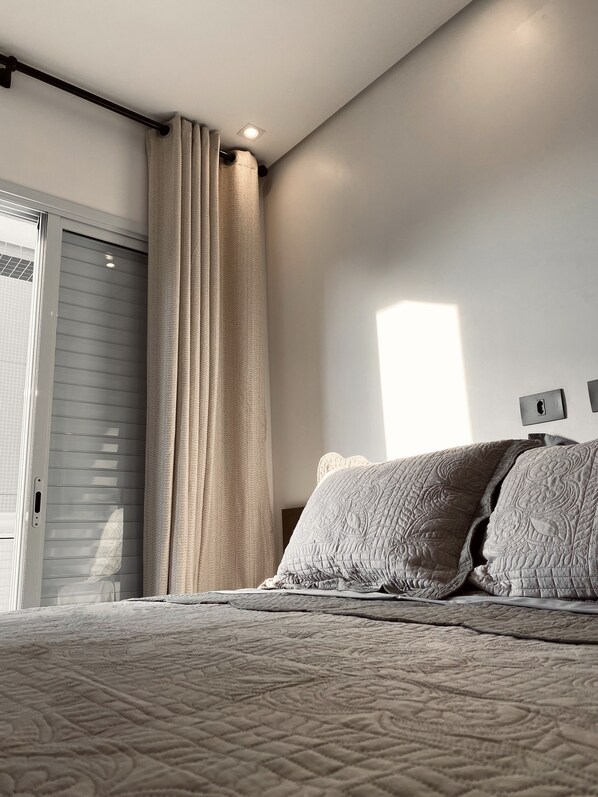 Quarto com cama, cortinas, luminária no teto e janela.