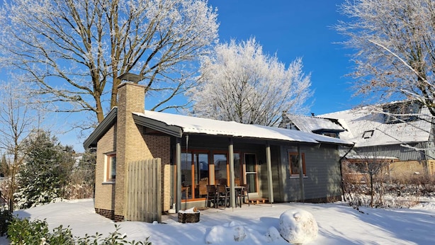 A house with a brick chimney, wooden deck, and snow-covered surroundings.
