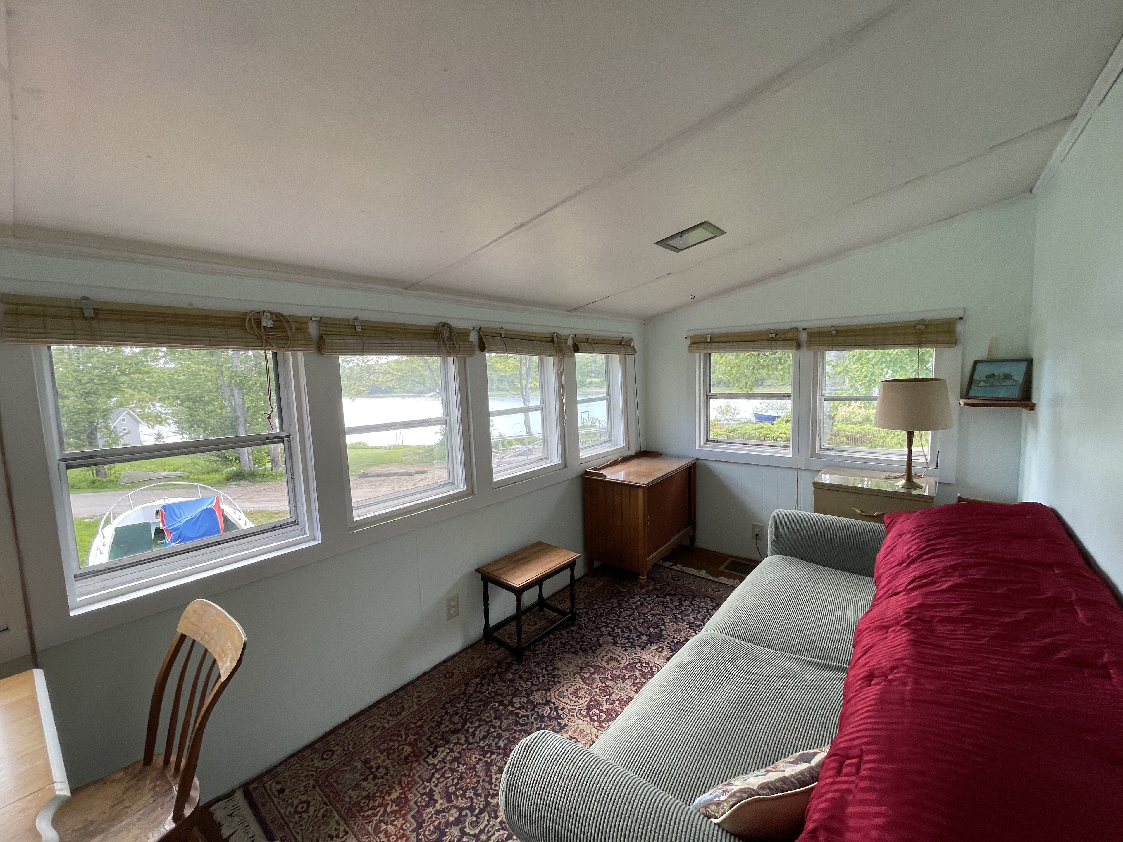 A room with a bed, a desk, a chair, and a window with a view of a lake.