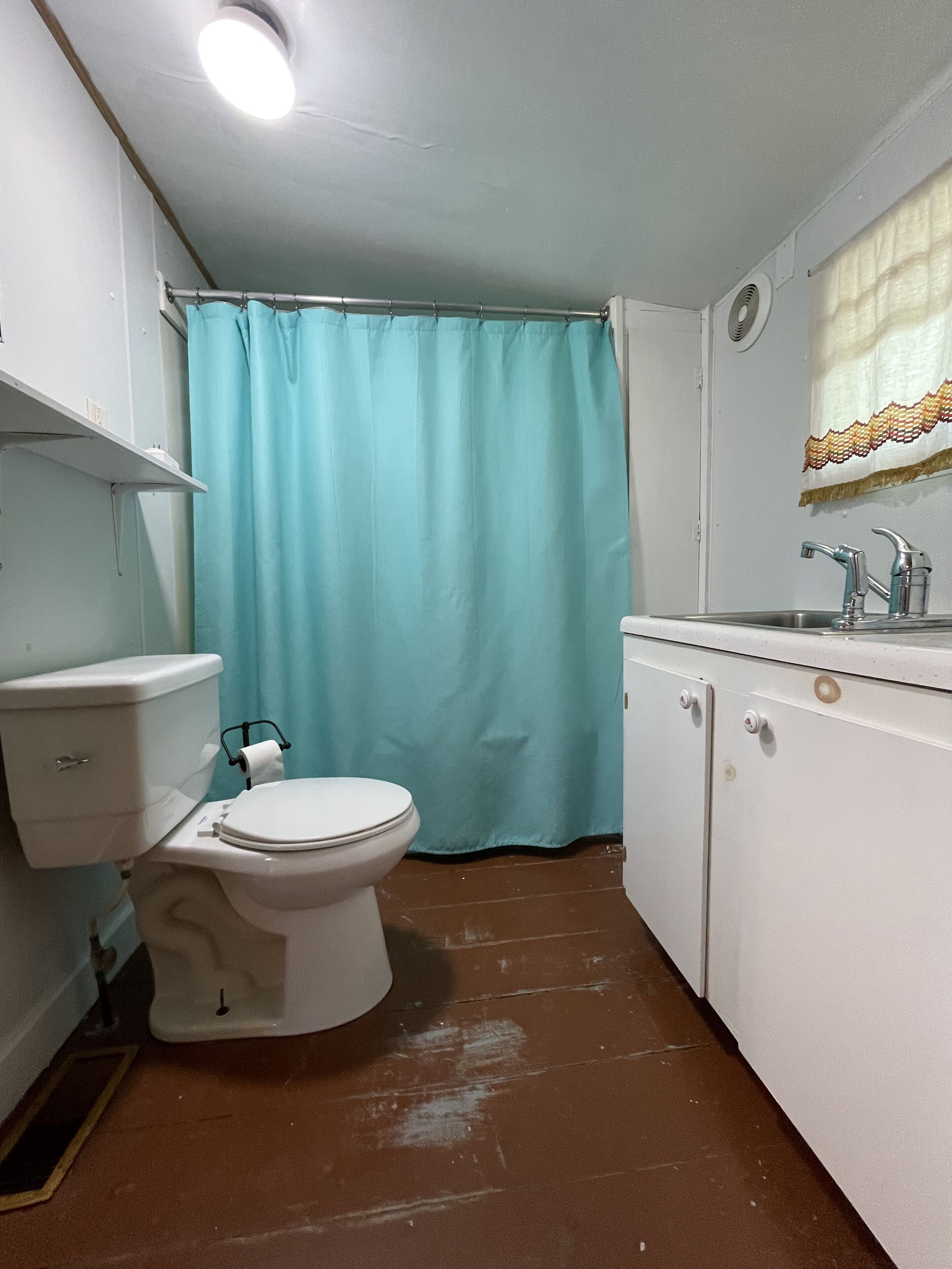 A small, compact bathroom with a white toilet, a blue shower curtain, and a sink with a faucet.