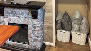 Sala de estar com lareira de pedra, televisão de tela plana na parede e estante com cestos e sacos.