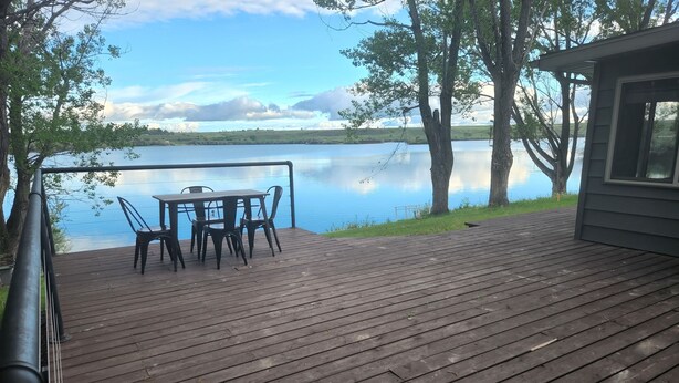 A wooden deck with a table and chairs overlooking a calm lake. - Beautiful 4 bedroom lake house with private dock. (Nashua)