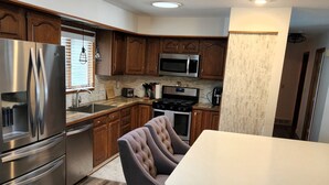 A modern kitchen with stainless steel appliances, wooden cabinets, and a bar area with stools. - Beautiful 4 bedroom lake house with private dock. (Nashua)