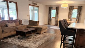 A spacious living room with a large sofa, a coffee table, and a dining area with a table and chairs. - Beautiful 4 bedroom lake house with private dock. (Nashua)