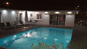 A swimming pool with lounge chairs and a table, surrounded by a covered patio area with sliding glass doors.