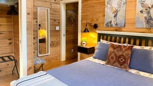 Ein Zimmer aus Holz mit einem Bett, einem Nachttisch, einer Lampe und zwei Bildern von Hirschen.