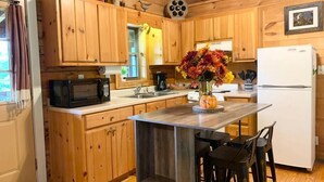 Eine Küchenzeile im Chalet-Stil mit Holzschränken, einer Mikrowelle, einem Spülbecken, einem Kühlschrank und einer Theke mit Hockern.