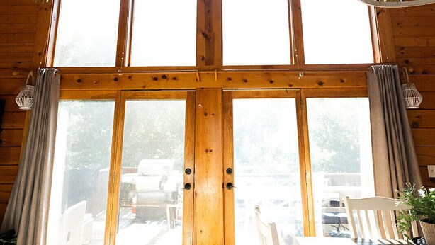 Una cabaña de madera con techo alto, ventanas grandes y un comedor con mesa y sillas.