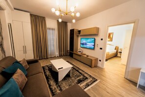 A modern living room with a sofa, coffee table, TV, and a dining area with a table and chairs.