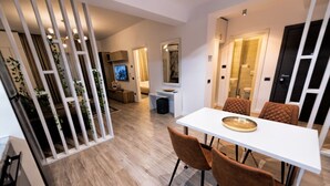 Un espace repas moderne avec une table blanche et des chaises marron, une cuisine en arrière-plan et une barrière végétale décorative.