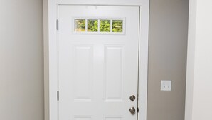 A white door with a window, a black doormat, and a wooden floor.