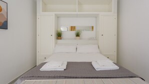 Quarto com cama, guarda-roupa branco e espelho sobre a cama.