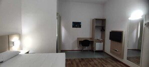 A hotel room with a bed, a desk, a chair, a small refrigerator, a wardrobe, a mirror, and a wall-mounted TV. - Italian Hotel (Parauapebas)