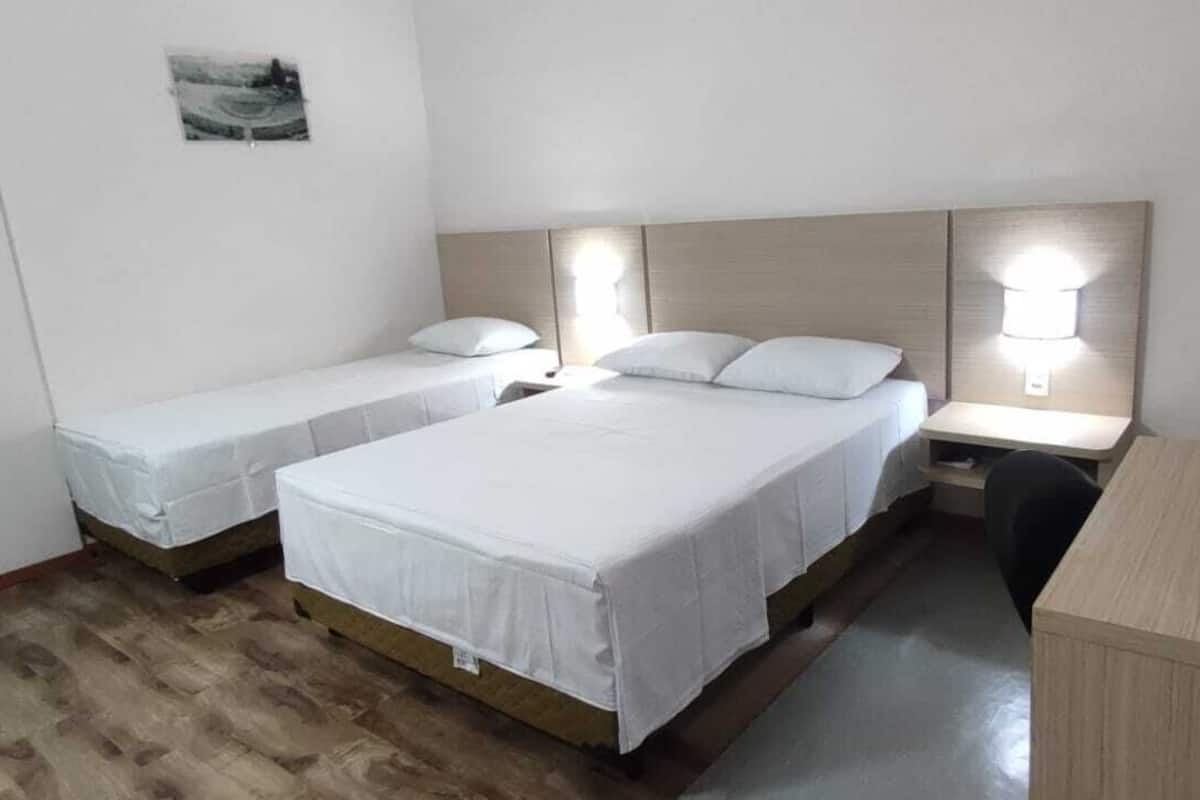 A room with two single beds and one double bed, wooden flooring, a desk, and a chair.