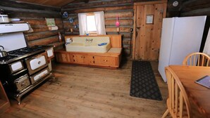 A rustic cabin-style kitchen with a wooden stove, sink, and a wooden bench.