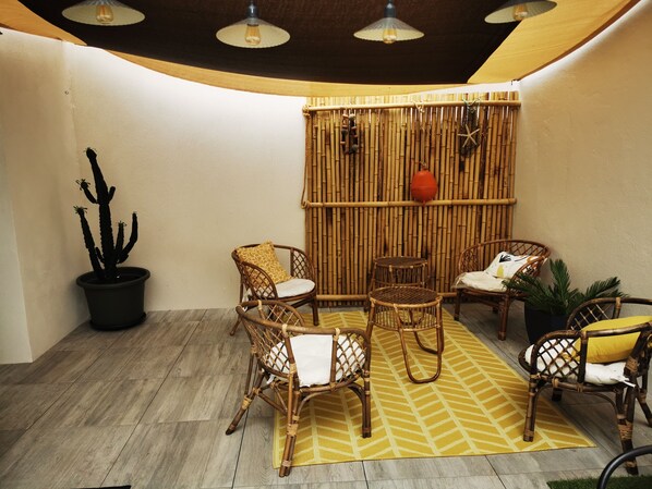Un patio acogedor con mobiliario de mimbre, un muro de bambú y una maceta con un cactus.