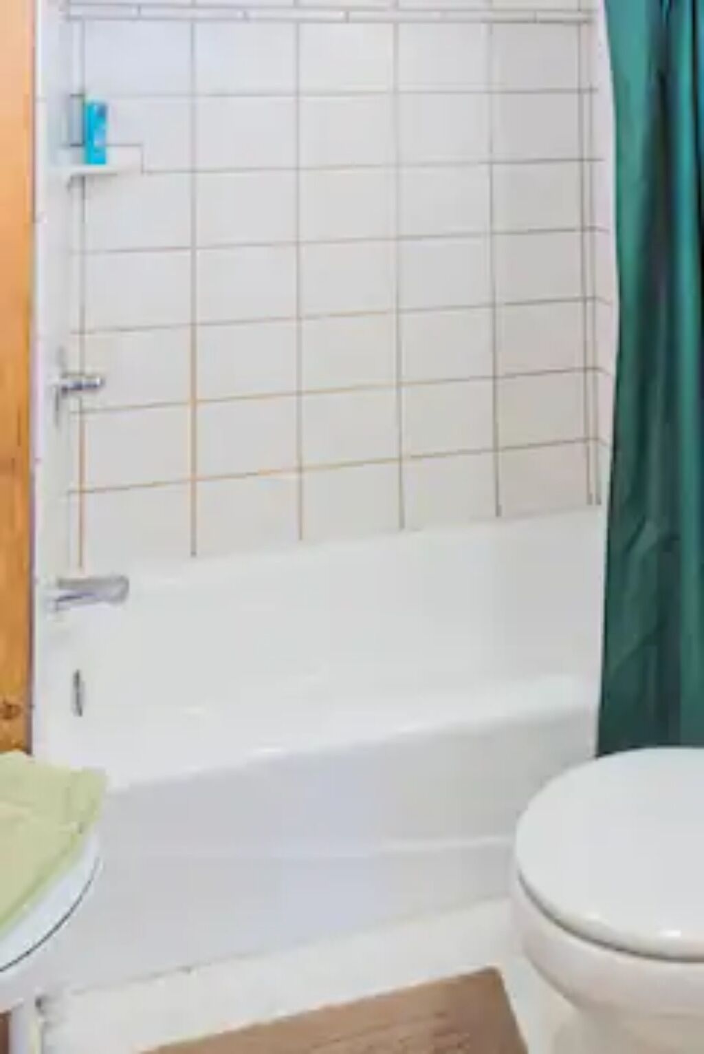 A bathroom with a white bathtub, a toilet, and a green shower curtain.