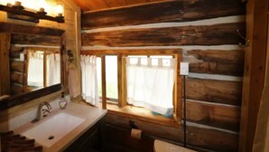 A rustic cabin bathroom with a wooden interior, a sink, a mirror, and a window with curtains. - Porcupine Cabin - A Classy-Rustic Gem (Clark)