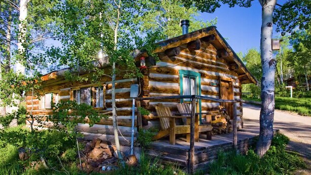 A log cabin with a porch, surrounded by trees and greenery. - Porcupine Cabin - A Classy-Rustic Gem (Clark)