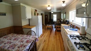A kitchen with wooden flooring, a dining table with chairs, a refrigerator, a stove, and a window with a view. - Caron House - A Well-Equipped Square Log Cabin! (Clark)