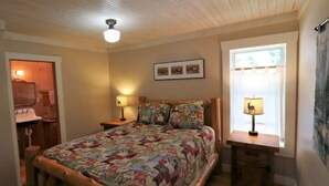 A bedroom with a wooden bed, two bedside lamps, a window with curtains, and a ceiling fan. - Caron House - A Well-Equipped Square Log Cabin! (Clark)