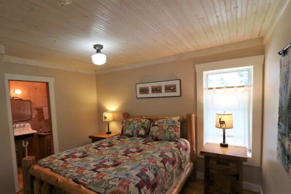 A bedroom with a wooden bed, two bedside lamps, a window with curtains, and a ceiling fan.