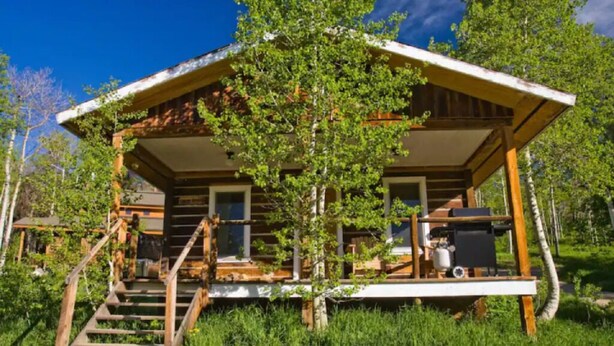 A rustic cabin with a wooden exterior, a porch with steps, and a small outdoor area with a grill. - Caron House - A Well-Equipped Square Log Cabin! (Clark)