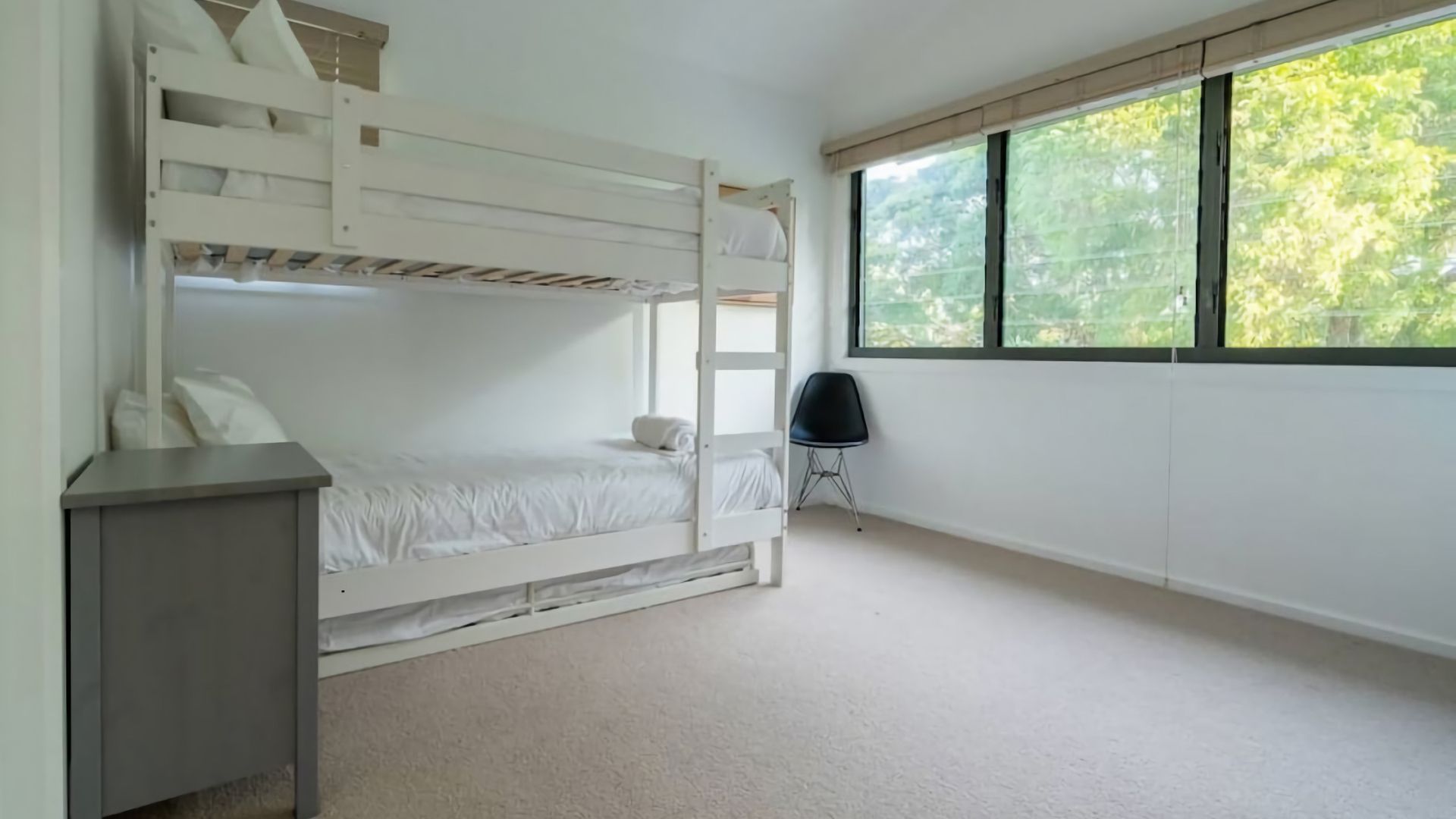 A bunk bed room with a desk, a chair, and a window with a view of trees.