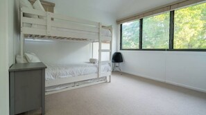 A bunk bed room with a desk, a chair, and a window with a view of trees. - Absolute Waterfront Beach House (Minnamurra)