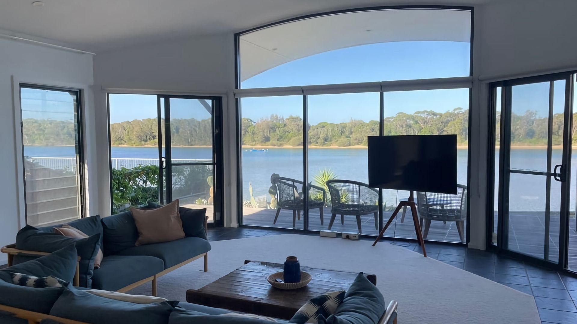 A spacious living area with a large window overlooking a lake, furnished with a sofa, chairs, and a coffee table.