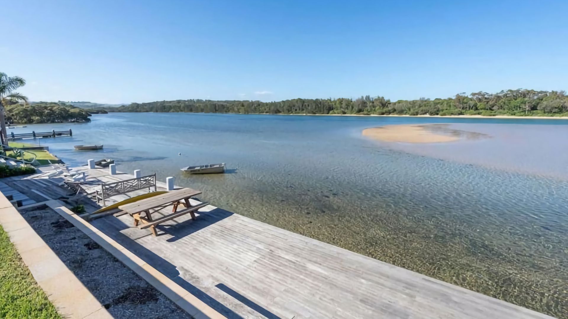 A wooden dock with picnic tables and a boat in a calm lake.