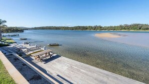 A wooden dock with picnic tables and a boat in a calm lake. - Absolute Waterfront Beach House (Minnamurra)