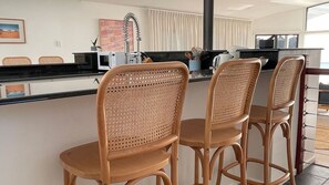 A kitchen with a black countertop, a white sink, and a stainless steel range hood. There are two wicker chairs with a woven backrest. - Absolute Waterfront Beach House (Minnamurra)
