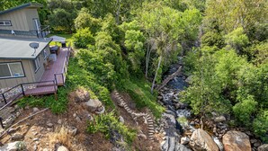 A house with a deck, a stone pathway, and a stream. - The River's Edge - Private Home with River Access, Spa, and Karaoke (Three Rivers)