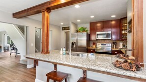 A modern kitchen with granite countertops, stainless steel appliances, and wooden bar stools. - The River's Edge - Private Home with River Access, Spa, and Karaoke (Three Rivers)