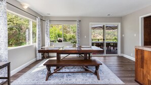 A spacious dining area with a large wooden table, benches, and a view of the outdoors through large windows. - The River's Edge - Private Home with River Access, Spa, and Karaoke (Three Rivers)