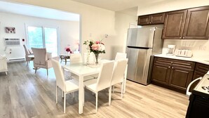 Una cocina moderna con refrigerador de acero inoxidable, gabinetes de madera y un comedor con sillas blancas y una mesa de vidrio.