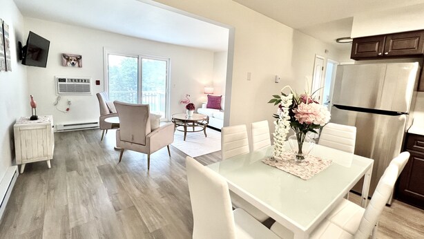 Una cocina moderna con armarios blancos, un refrigerador de acero inoxidable y un comedor con mesa de vidrio y sillas blancas.