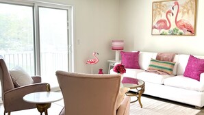 Una sala de estar con un sofá blanco, sillones rosa, una mesita de centro redonda y un cuadro de flamencos.